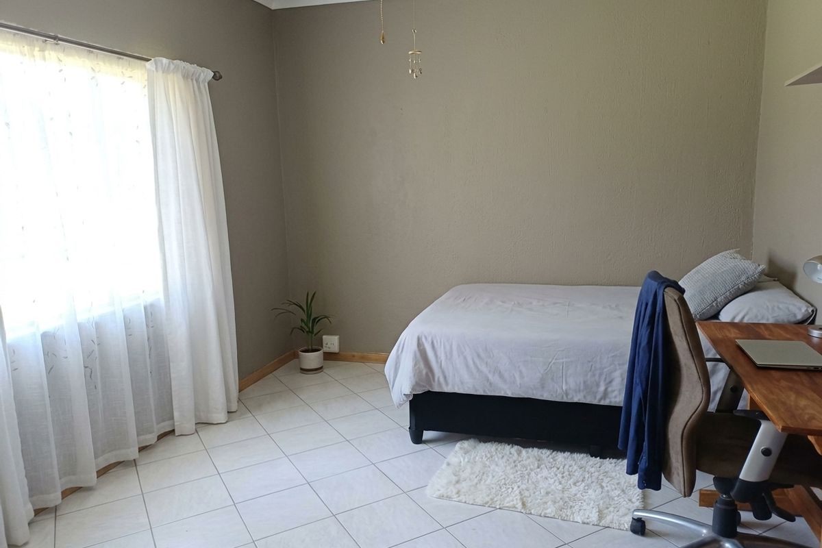 A functional bedroom featuring neutral wall tones, tiled flooring, and natural light through a large window.