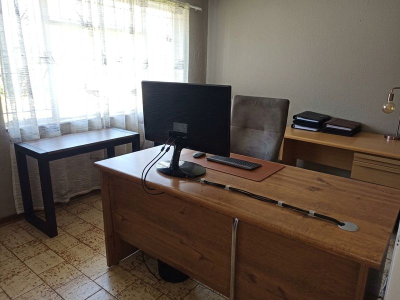 A functional home office space featuring tiled flooring and natural light from a large window, suitable for a dedicated workspace.