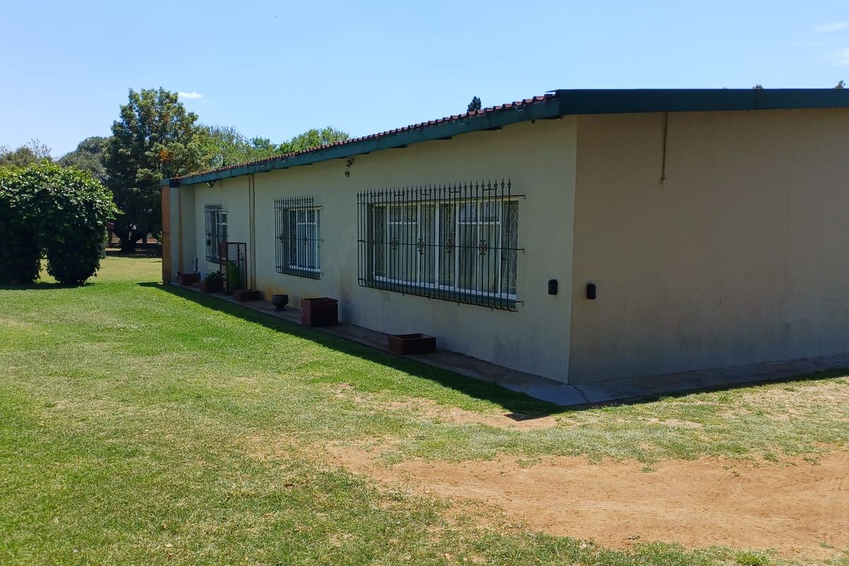 Rear exterior view of the house featuring a simple facade with security bars on windows and a surrounding lawn area.