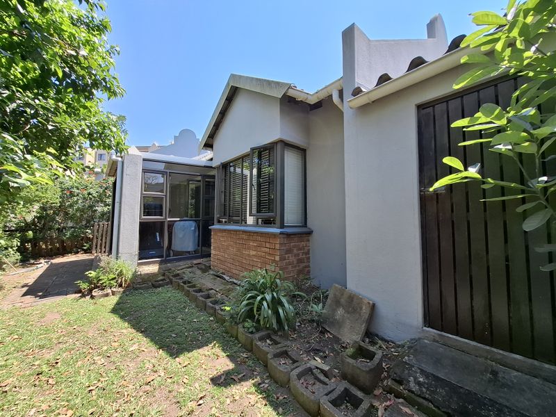 Rear exterior view of the townhouse featuring a brick and plaster facade, aluminium window frames, and a small garden area with paved access.