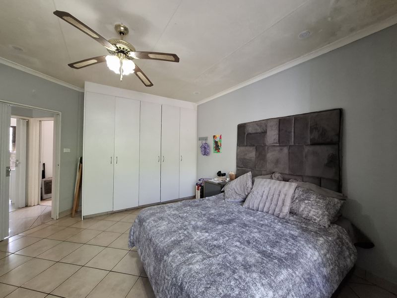 Spacious bedroom featuring tiled flooring, built-in cupboards, and a ceiling fan, with visible ceiling staining requiring attention.