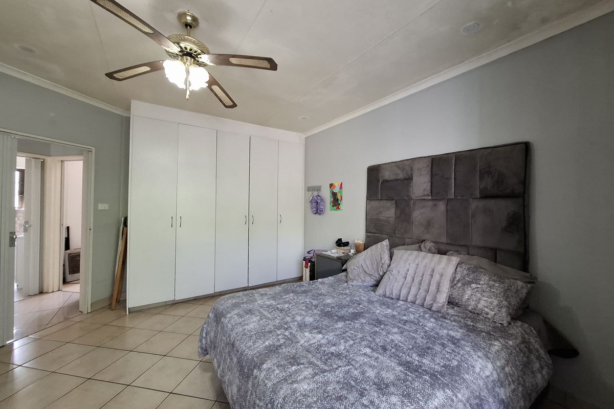 Spacious bedroom featuring tiled flooring, built-in cupboards, and a ceiling fan, with visible ceiling staining requiring attention.
