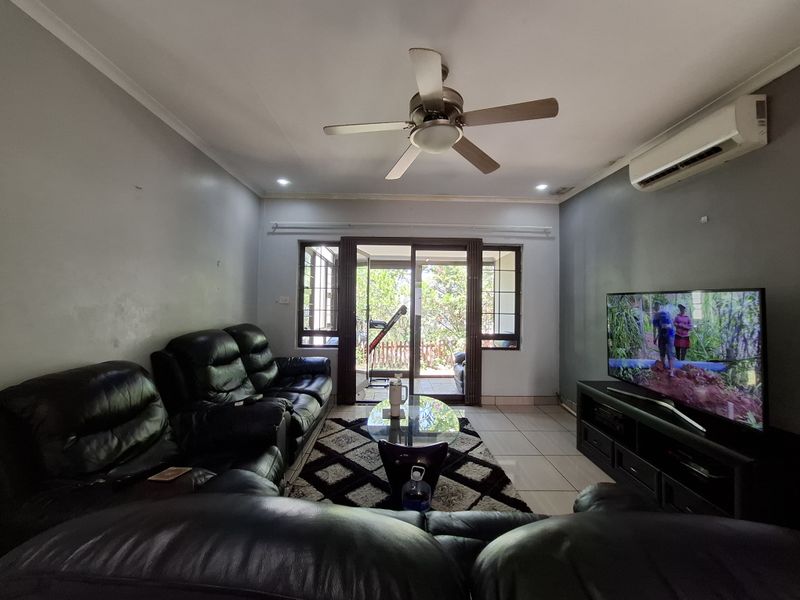 A comfortable living room featuring tiled flooring, a ceiling fan, and a split-system air conditioner, with direct access to an outdoor patio area.