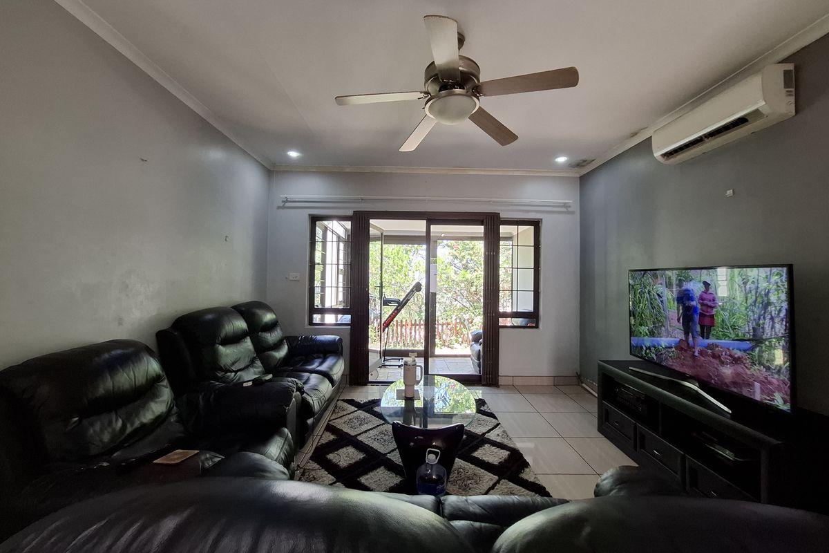 A comfortable living room featuring tiled flooring, a ceiling fan, and a split-system air conditioner, with direct access to an outdoor patio area.