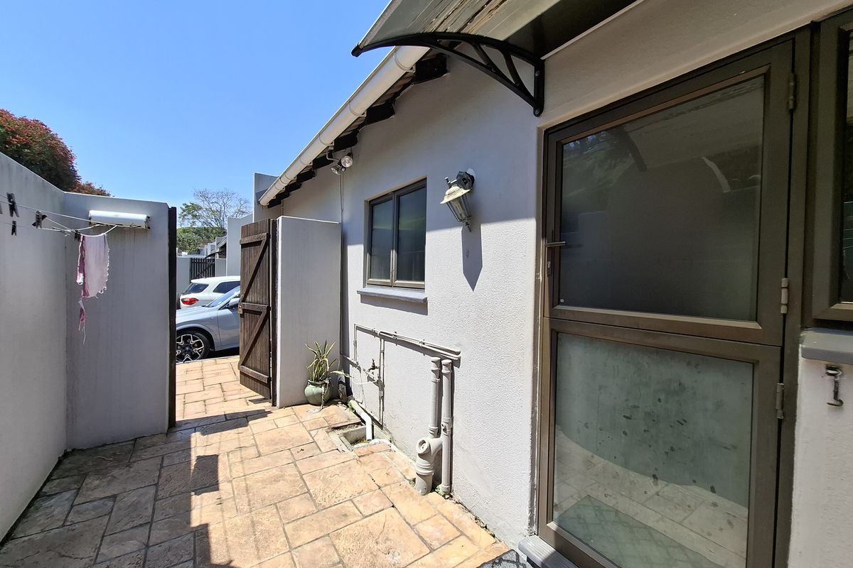 A paved rear courtyard area featuring an external door, wall-mounted lighting, and an awning, providing a functional outdoor utility space.