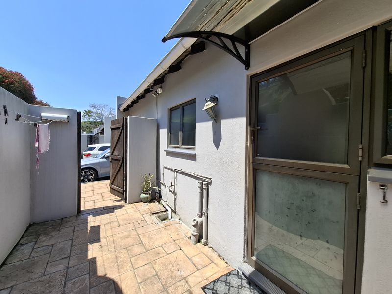 A paved rear courtyard area featuring an external door, wall-mounted lighting, and an awning, providing a functional outdoor utility space.