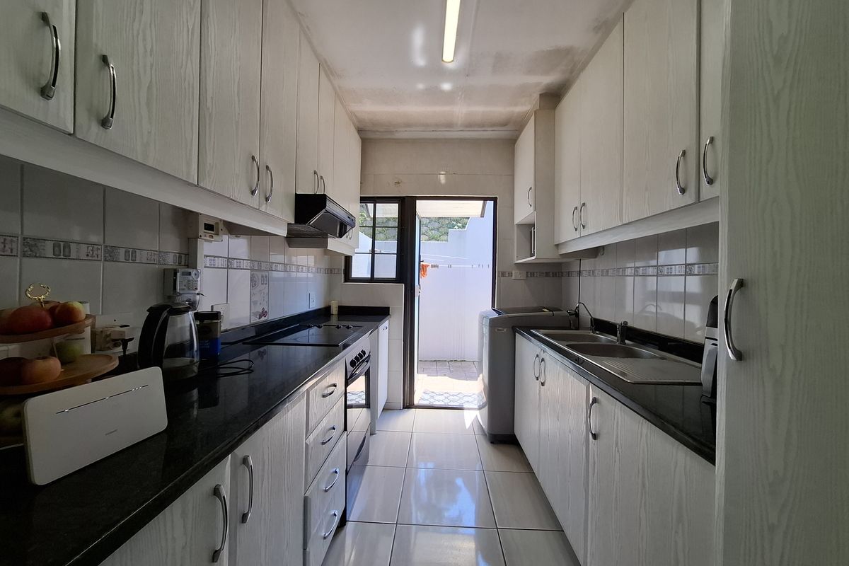 Galley-style kitchen featuring granite countertops, built-in cabinetry, and integrated appliances, with direct access to an outdoor area.