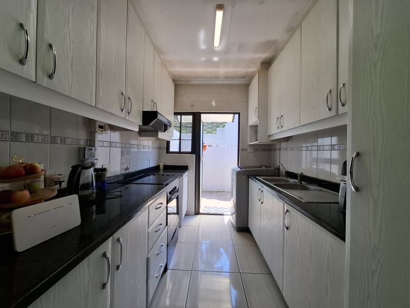 Galley-style kitchen featuring granite countertops, built-in cabinetry, and integrated appliances, with direct access to an outdoor area.