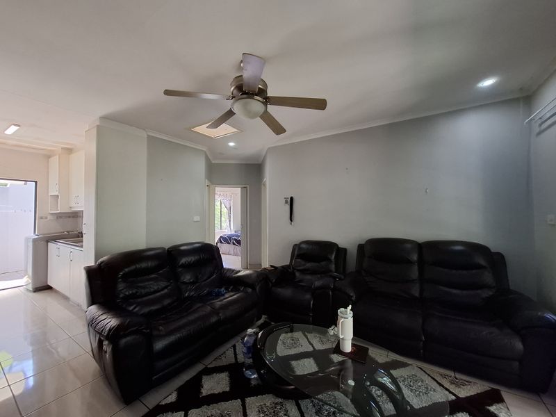 Open plan living area featuring tiled floors, ceiling fan, and recessed lighting, with an adjacent kitchen and view into a bedroom.