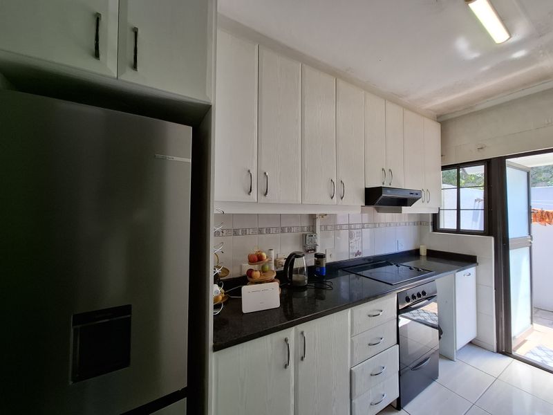 A functional kitchen featuring white cabinetry, dark granite countertops, built-in oven, electric hob, and direct access to an outdoor area.