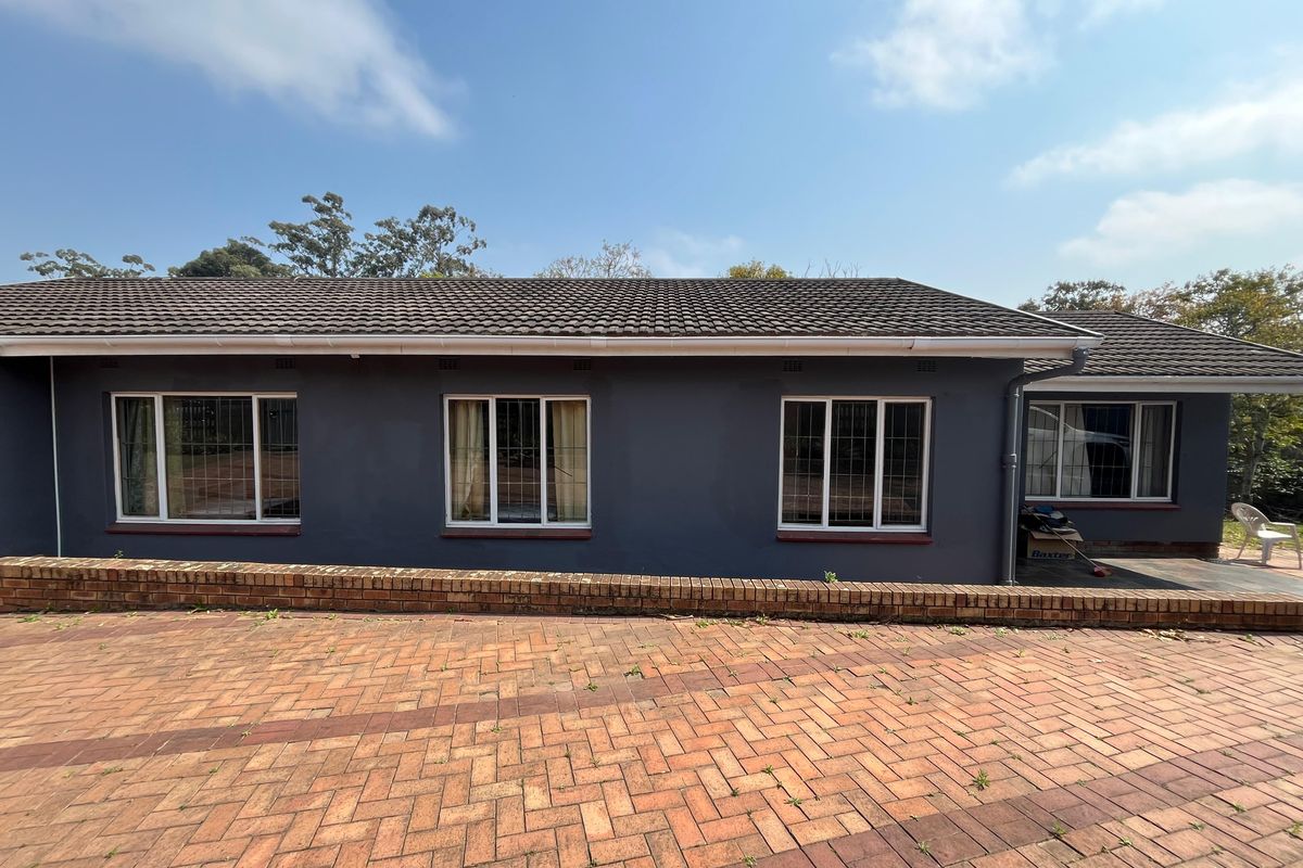 Rear exterior view of the house featuring a dark grey facade, tiled roof, and a brick paved patio area with a low retaining wall.