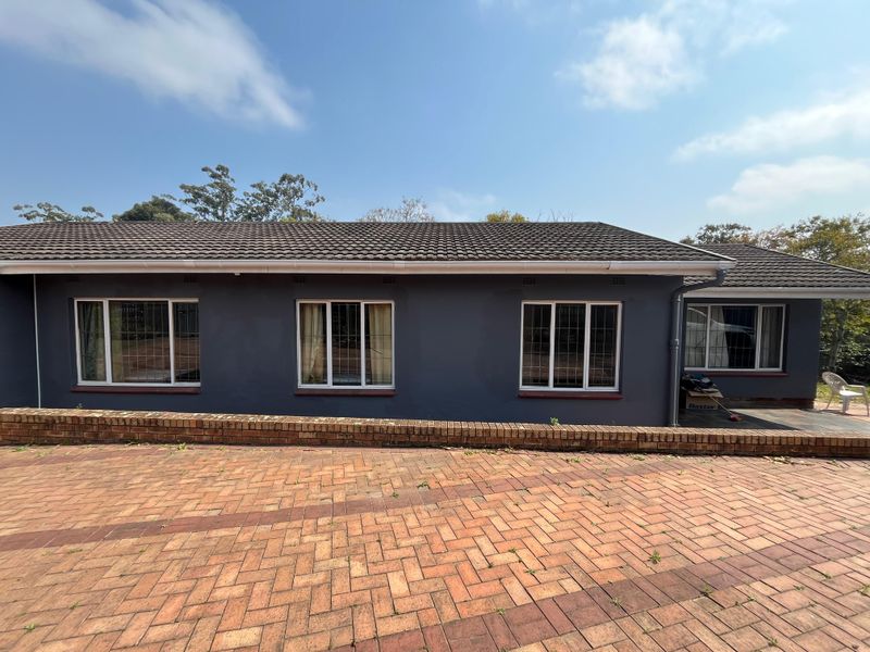 Rear exterior view of the house featuring a dark grey facade, tiled roof, and a brick paved patio area with a low retaining wall.