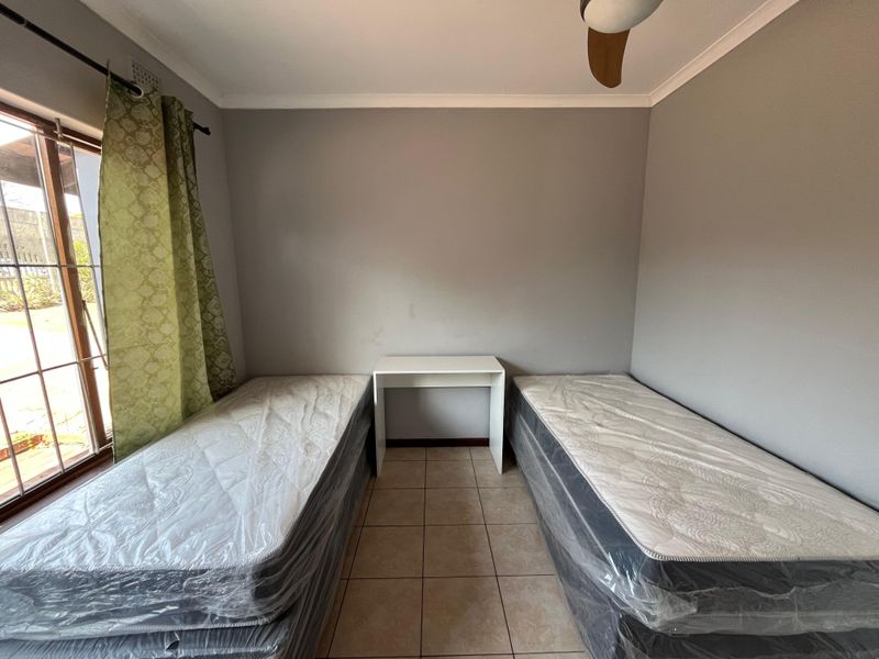 A functional bedroom featuring tiled flooring, a ceiling fan, and a sliding glass door providing natural light and outdoor access.