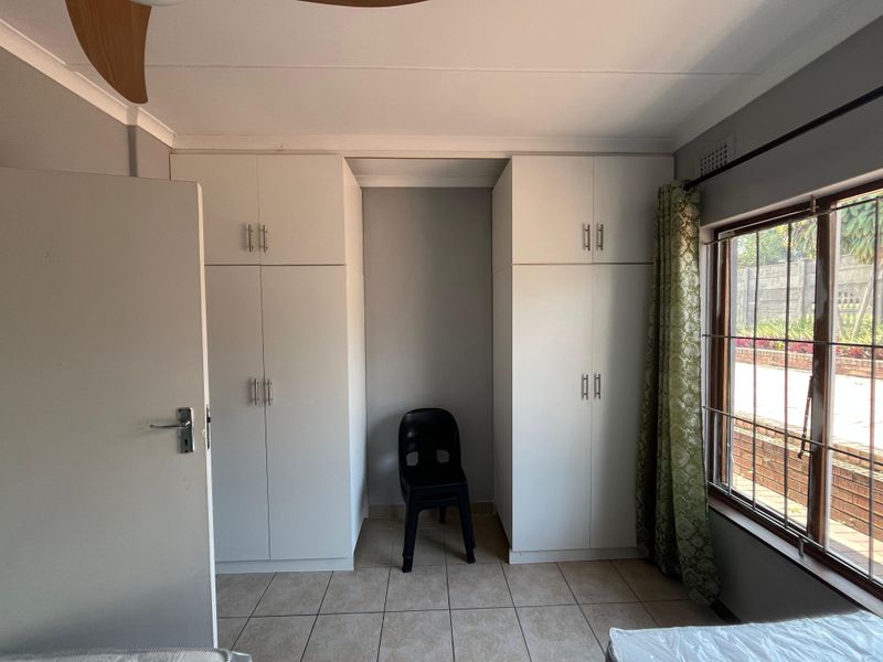 A bedroom featuring built-in cupboards, tiled flooring, and a ceiling fan, offering a functional and neutral space ready for personalization.