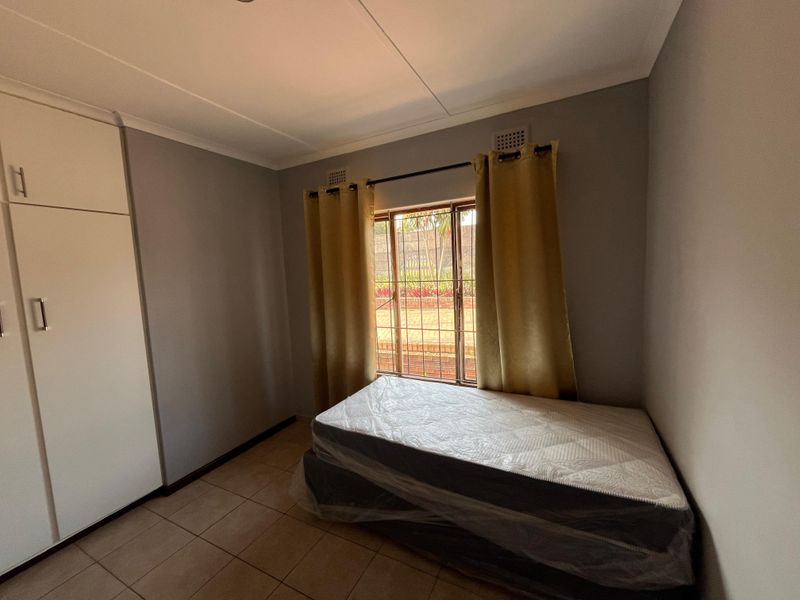 A functional bedroom featuring tiled flooring, built-in cupboards, and security bars on the window, providing a clean and neutral space.