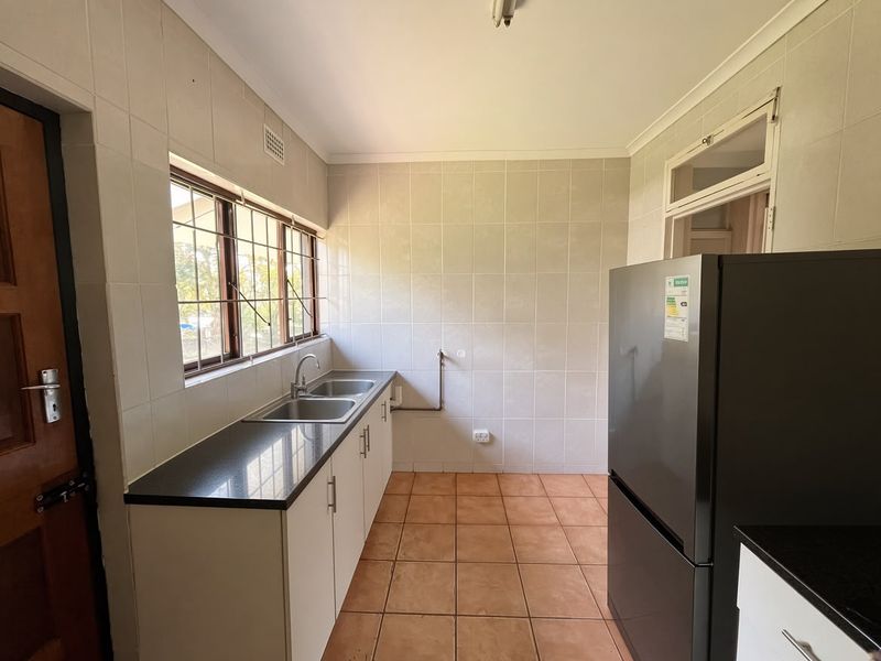 A functional scullery area featuring tiled walls, granite countertops, a double basin sink, and tiled flooring, providing a practical space for food preparation.