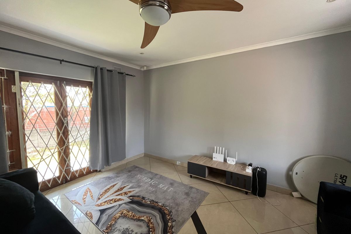 A bright living room featuring tiled flooring, a modern ceiling fan, and double doors with security gates leading to the exterior.