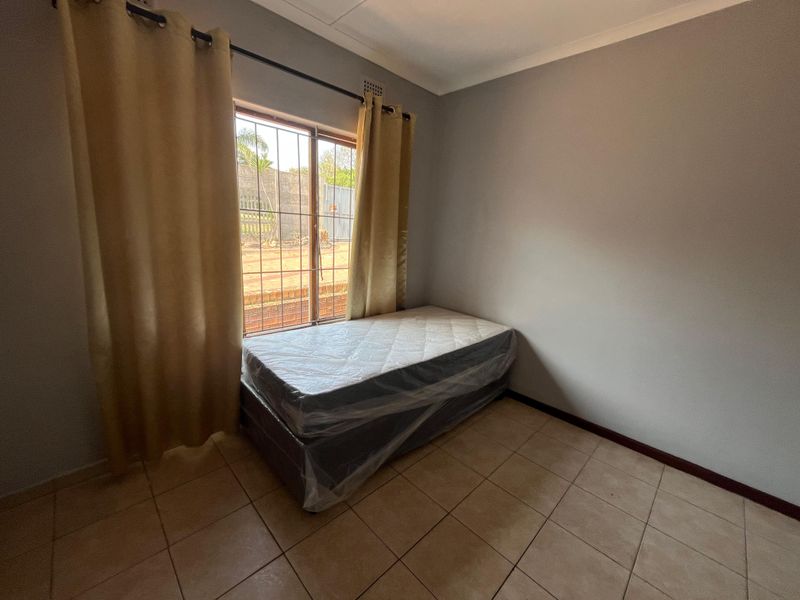 A simple bedroom featuring tiled flooring, neutral walls, and a window fitted with security bars.