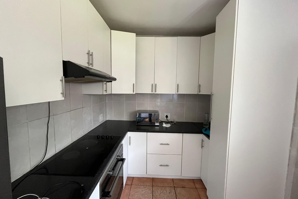 A functional kitchen featuring white cabinetry, black countertops, a built-in oven with hob, extractor fan, and tiled flooring.