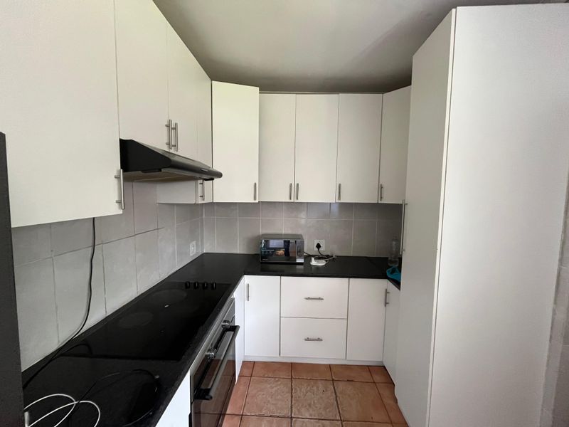 A functional kitchen featuring white cabinetry, black countertops, a built-in oven with hob, extractor fan, and tiled flooring.