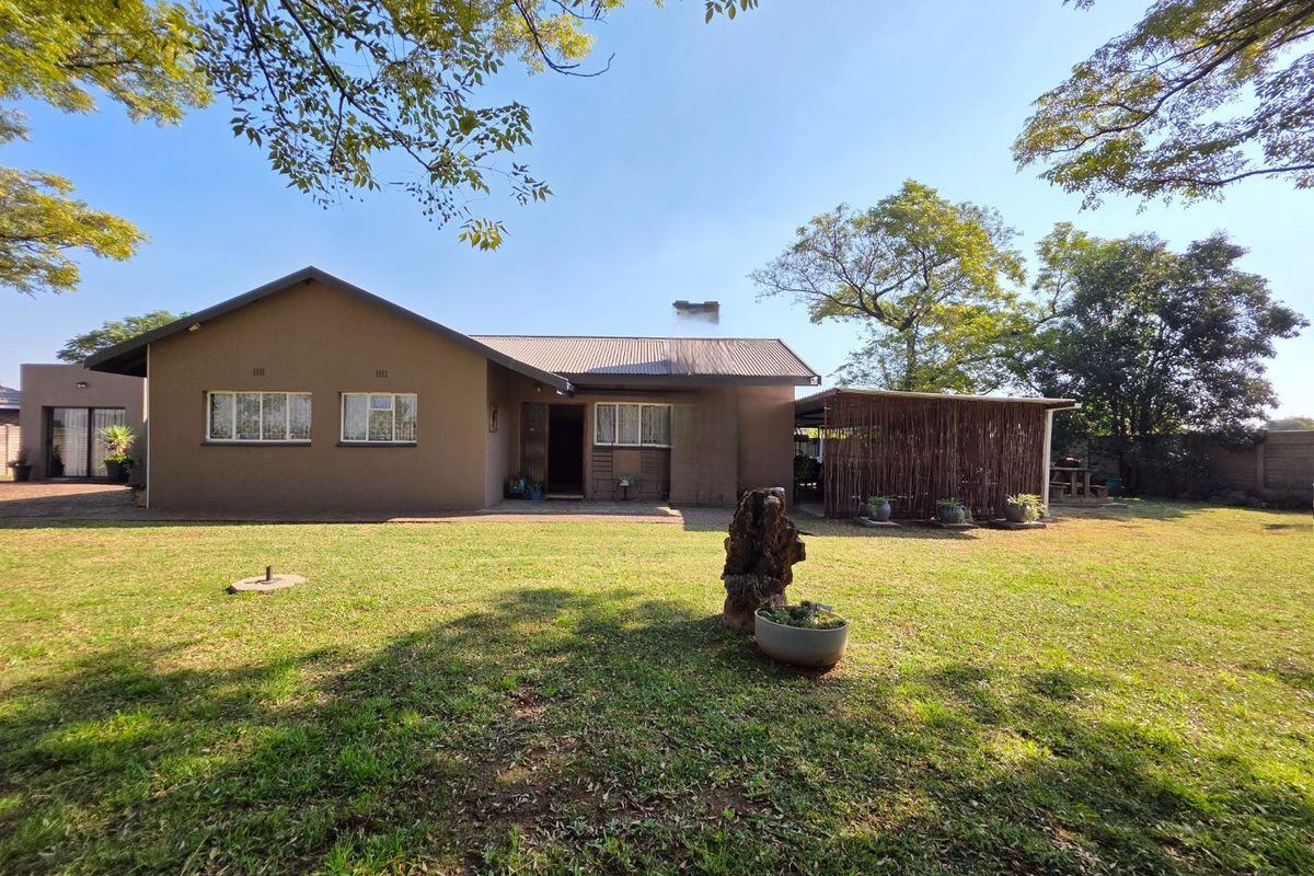 Rear view of the house featuring a spacious lawn, brick facade, corrugated metal roof, and a covered patio area.