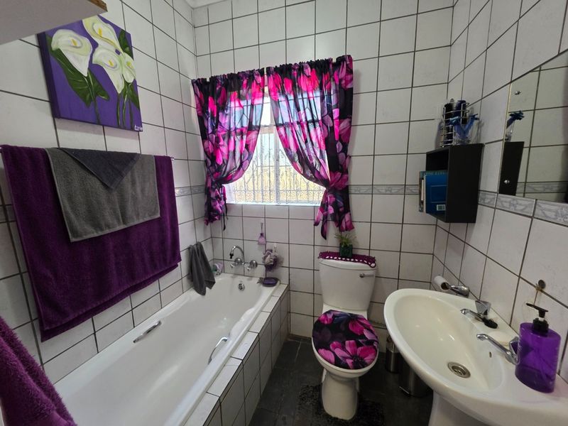 A functional bathroom featuring a built-in bathtub, pedestal washbasin, and toilet, finished with full-height wall tiling.