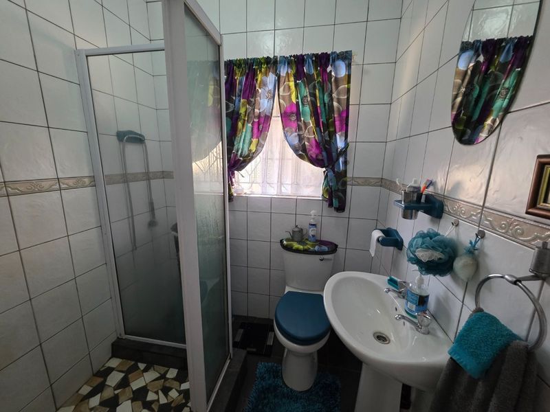 A functional bathroom featuring a shower enclosure, pedestal basin, and toilet with full-height wall tiling.