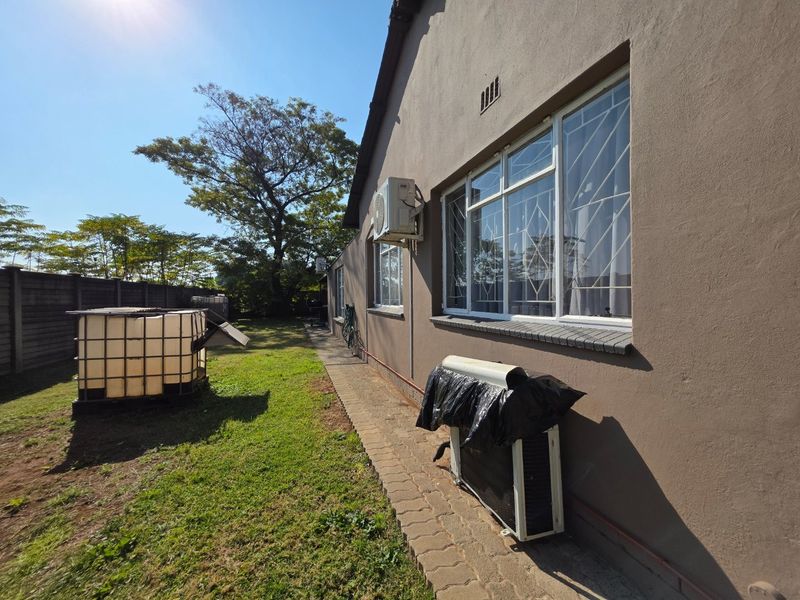 Rear exterior view of the property featuring a paved walkway, lawn area, and wall-mounted air conditioning units.