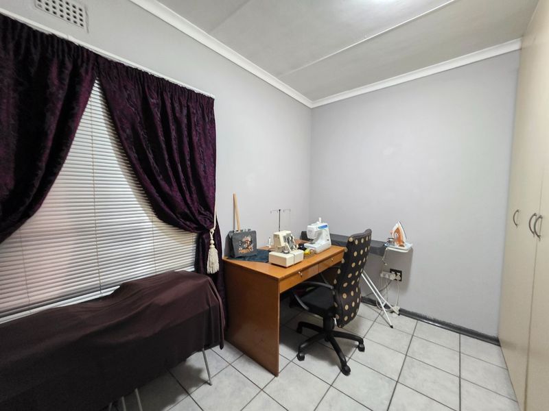 A functional bedroom featuring tiled flooring, a built-in wardrobe, and neutral wall finishes, currently utilized as a workspace.
