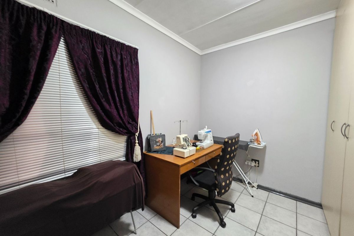 A functional bedroom featuring tiled flooring, a built-in wardrobe, and neutral wall finishes, currently utilized as a workspace.