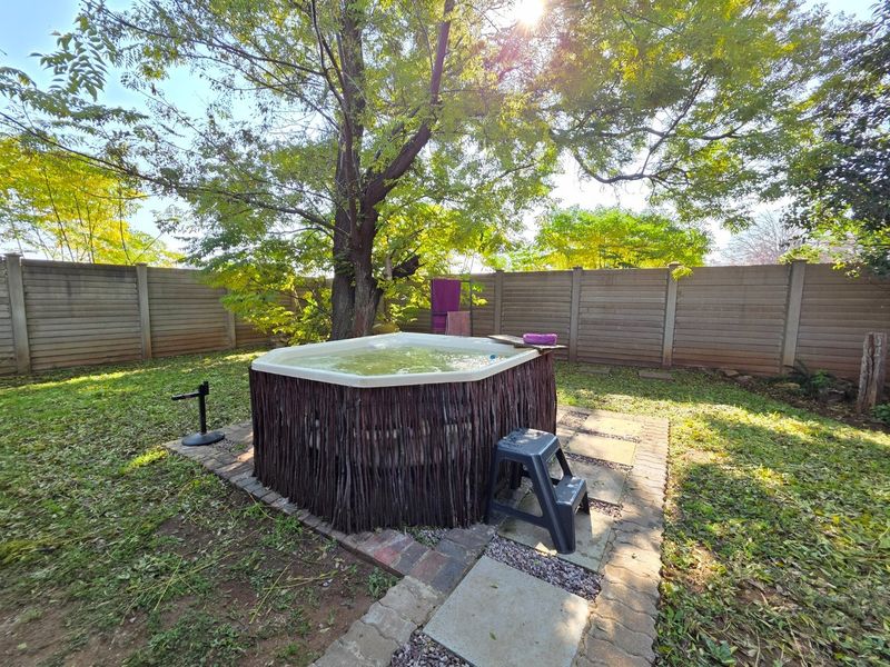 Outdoor garden area featuring a hot tub set on a paved base, enclosed by a precast concrete boundary wall and mature trees.