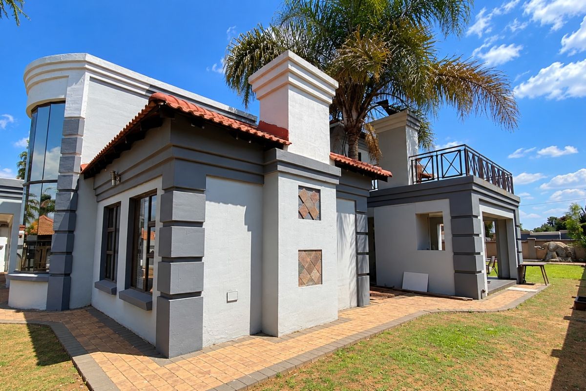 Rear view of the property featuring a paved patio area, a balcony with metal railings, and distinctive architectural detailing with terracotta roof tiles.