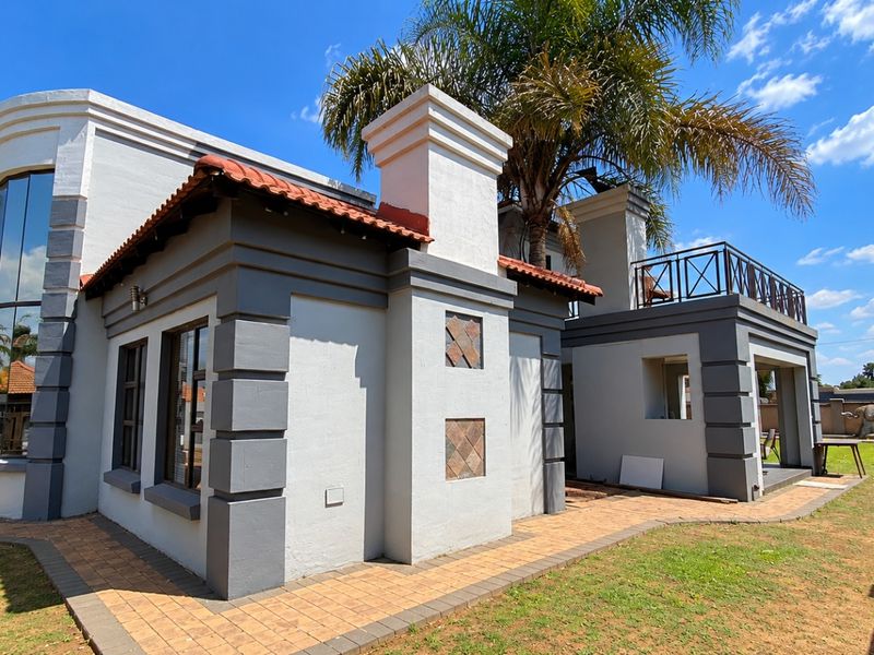 Rear view of the property featuring a paved patio area, a balcony with metal railings, and distinctive architectural detailing with terracotta roof tiles.