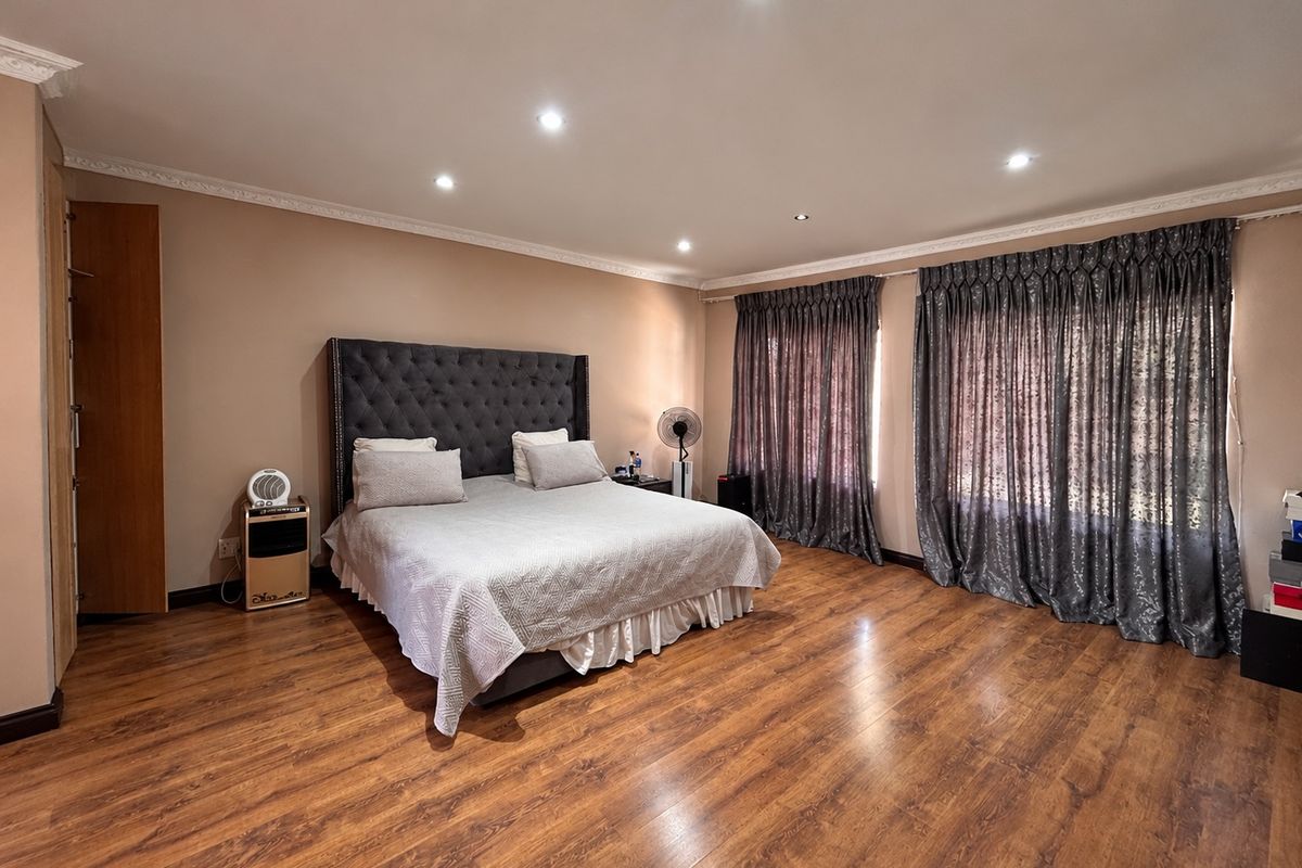 Spacious bedroom featuring warm laminate flooring, recessed downlighting, decorative crown molding, and a built-in cupboard.