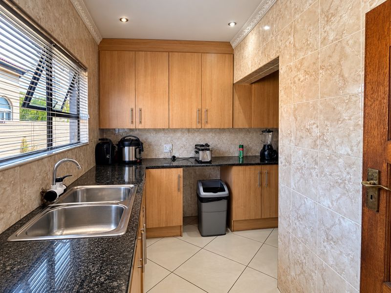 A functional scullery featuring granite countertops, double stainless steel sink, ample wooden cabinetry, and tiled finishes throughout.