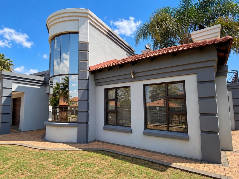 A modern residential exterior featuring a distinctive curved glass facade, terracotta roof tiles, and well-maintained paved walkways surrounding the property.