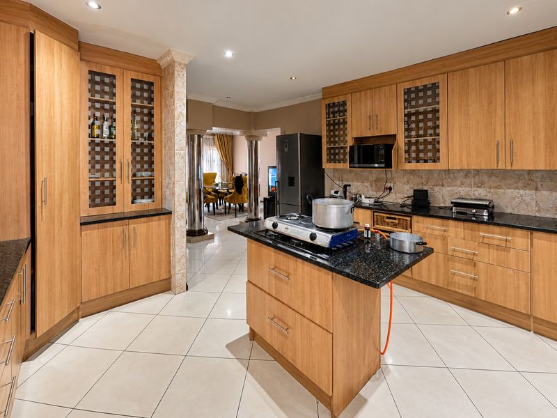Spacious kitchen featuring warm wood cabinetry, granite countertops, a central island, and tiled flooring, seamlessly flowing into the adjacent living area.