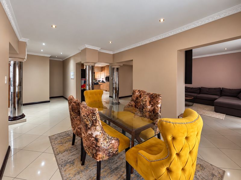 Spacious open-plan dining area featuring tiled floors, decorative ceiling cornices, and structural columns, seamlessly connecting to the kitchen and living room.