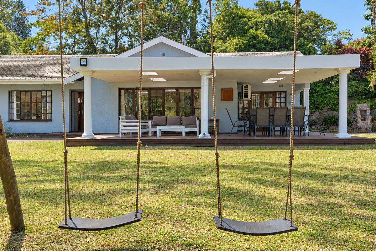Spacious rear exterior featuring a covered patio with timber decking, classic columns, and recessed lighting, overlooking a well-maintained garden.