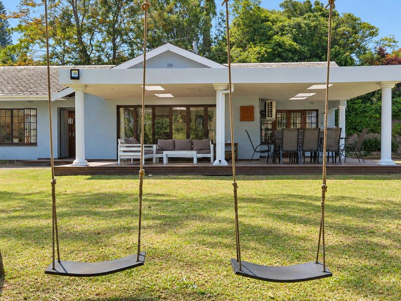 Spacious rear exterior featuring a covered patio with timber decking, classic columns, and recessed lighting, overlooking a well-maintained garden.