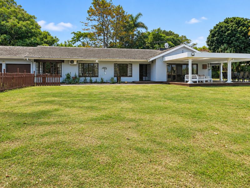 Spacious rear garden featuring a large lawn, a covered patio with wooden decking, and a well-maintained single-story residential facade.