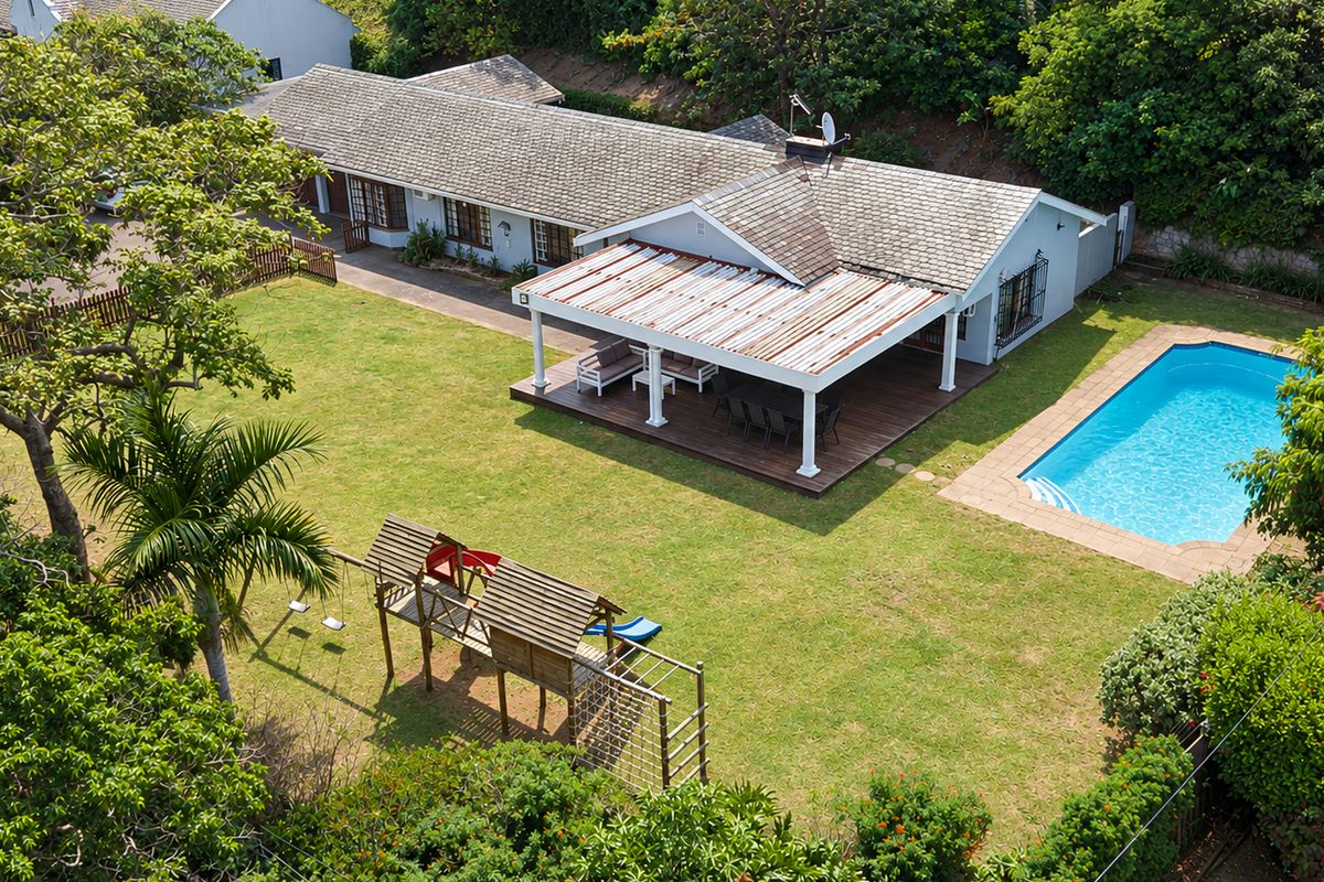 Aerial view of a residential property featuring a spacious lawn, a swimming pool, and a covered patio area with wooden decking.