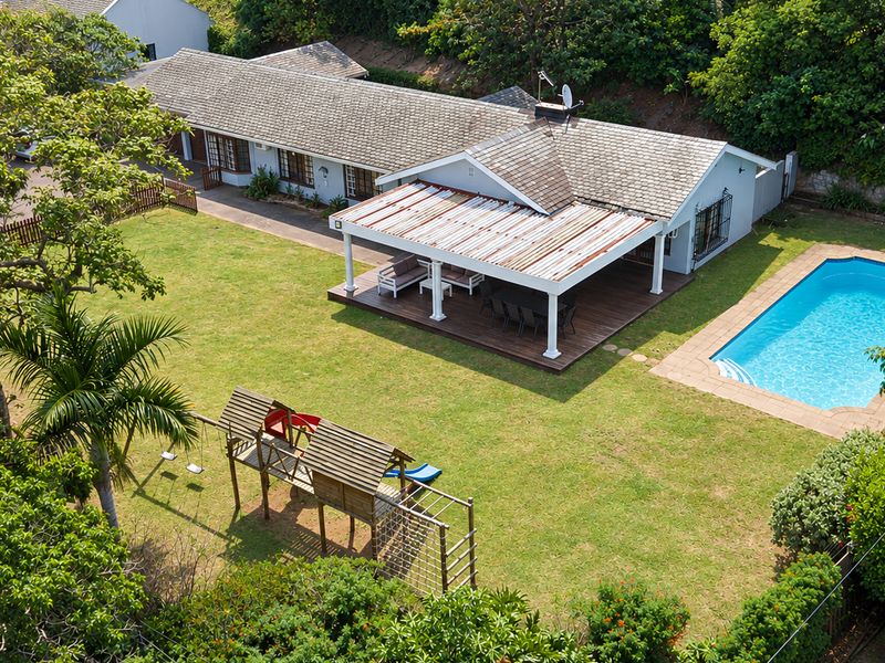 Aerial view of a residential property featuring a spacious lawn, a swimming pool, and a covered patio area with wooden decking.