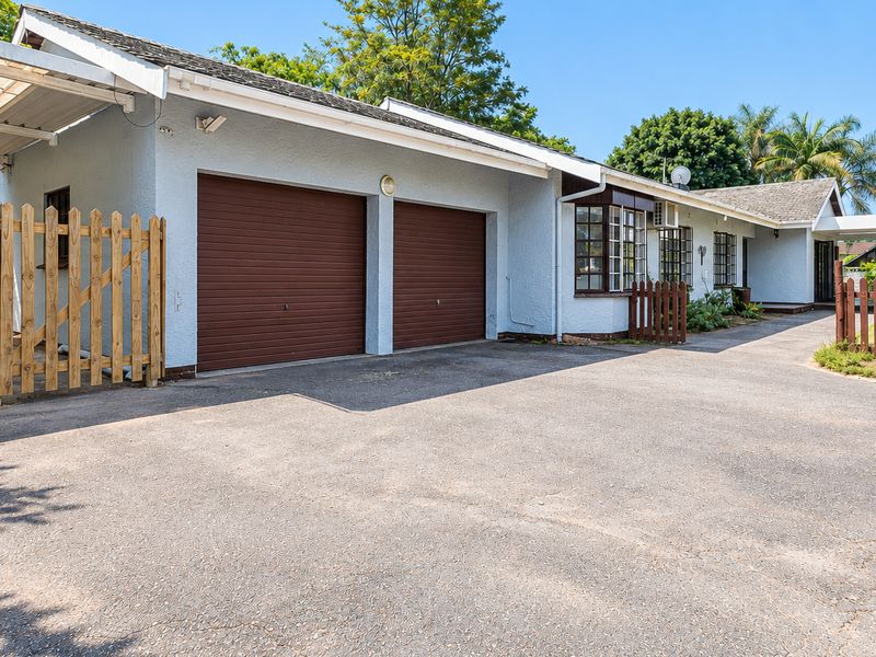 Front exterior view of the property featuring a double garage, paved driveway, carport, and timber fencing surrounding the garden area.