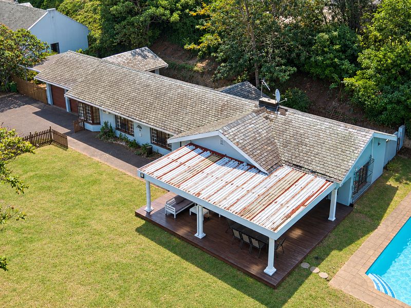 Aerial view of a residential property featuring a swimming pool, timber deck with a covered patio, and a shingle roof.