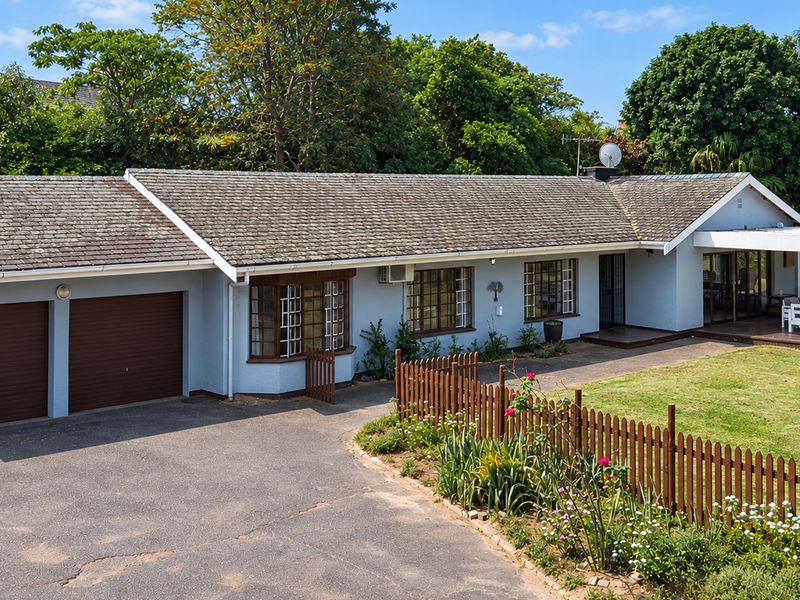 A well-maintained single-story residence featuring a double garage, paved driveway, bay window, and a covered patio overlooking the garden.