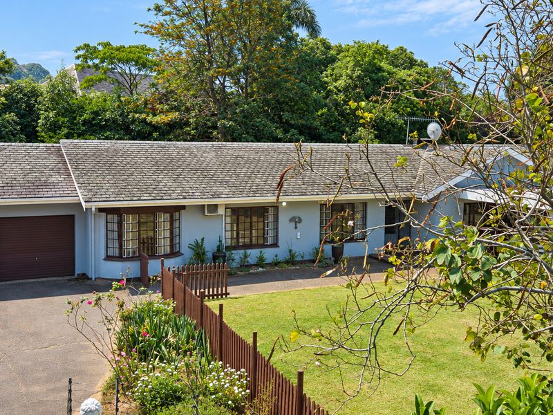 Front elevation of a single-story house featuring a double garage, paved driveway, bay window, and a well-maintained front garden with timber fencing.