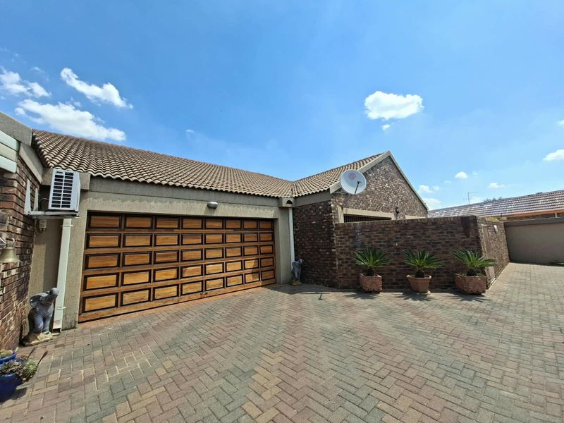 Front exterior view of the property featuring a brick facade, tiled roof, and a large wooden sectional garage door with a paved driveway.