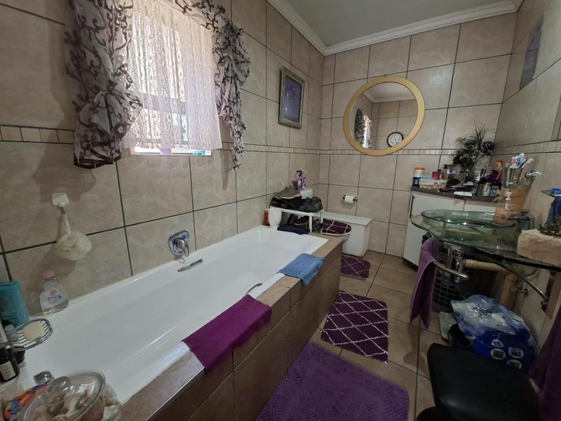 A functional bathroom featuring a built-in bathtub, tiled wall finishes, a glass vessel sink, and a toilet, offering a practical layout for daily use.