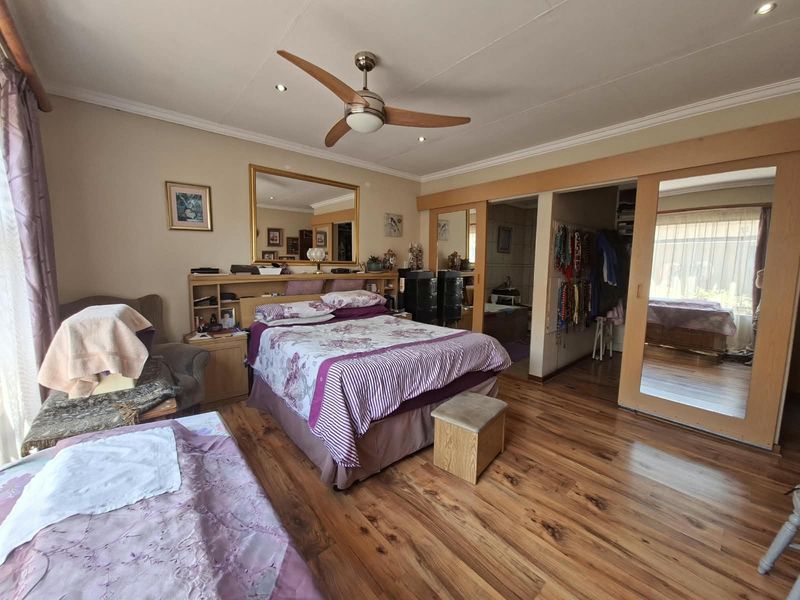 Spacious bedroom featuring laminate flooring, recessed lighting, a ceiling fan, and built-in wardrobes with mirrored sliding doors.